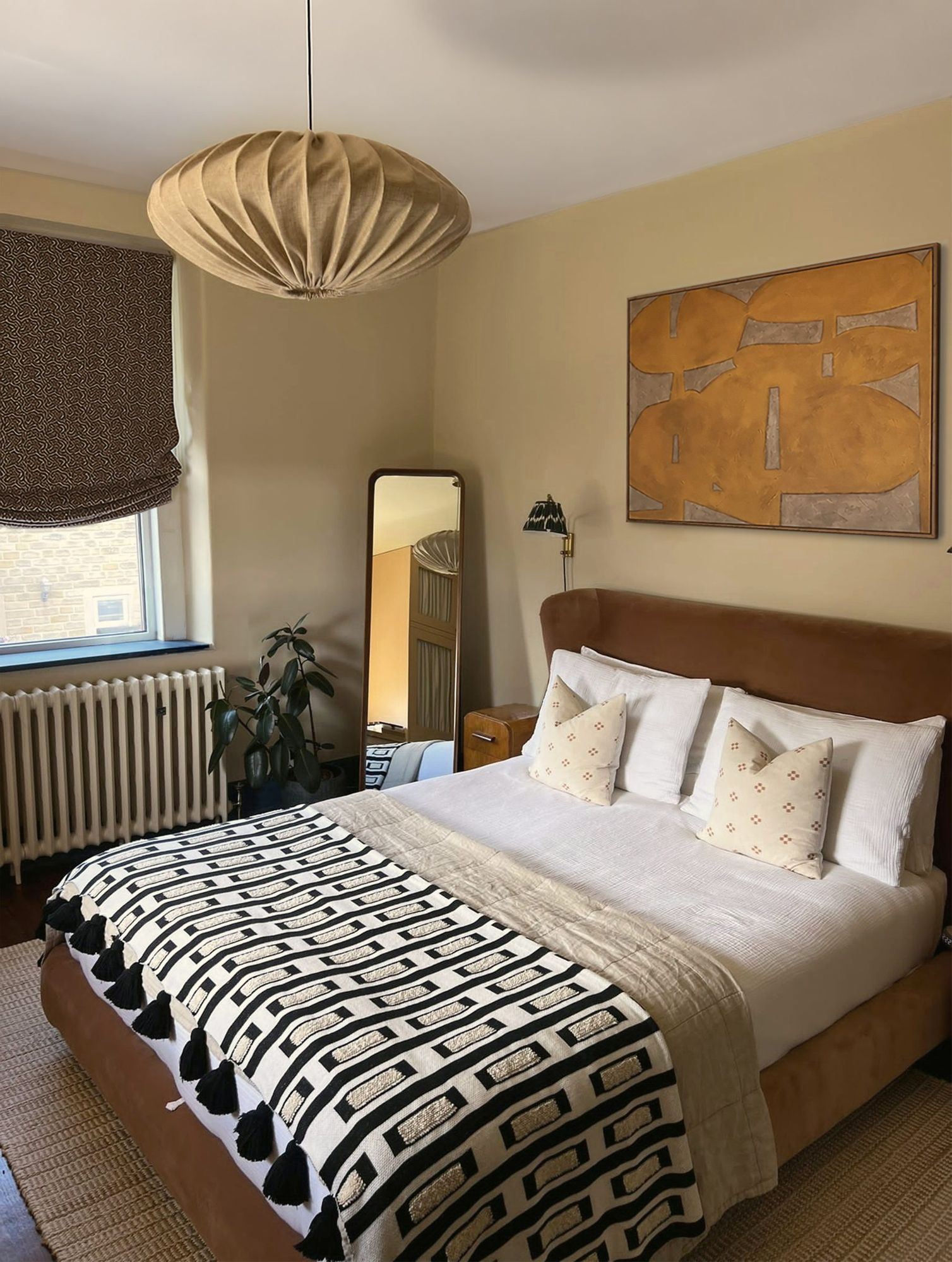 Bedroom with pleated pendant, velvet headboard and orange abstract artwork